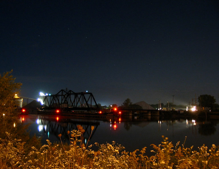 CSX Grand Haven Swing Bridge
The lights of the now stopped CSX D727 illuminate the Grand Haven swing bridge. Conductor is about to get out to turn the bridge into place. The train the heads across the bridge, with the brakeman in the Chessie caboose reopening the bridge for boat traffic.   Fall 2004
